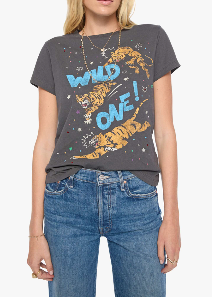 A woman wearing a dark gray graphic t-shirt with a colorful print of two tigers and the text 'WILD ONE!' in blue, paired with blue jeans against a light gray background.
