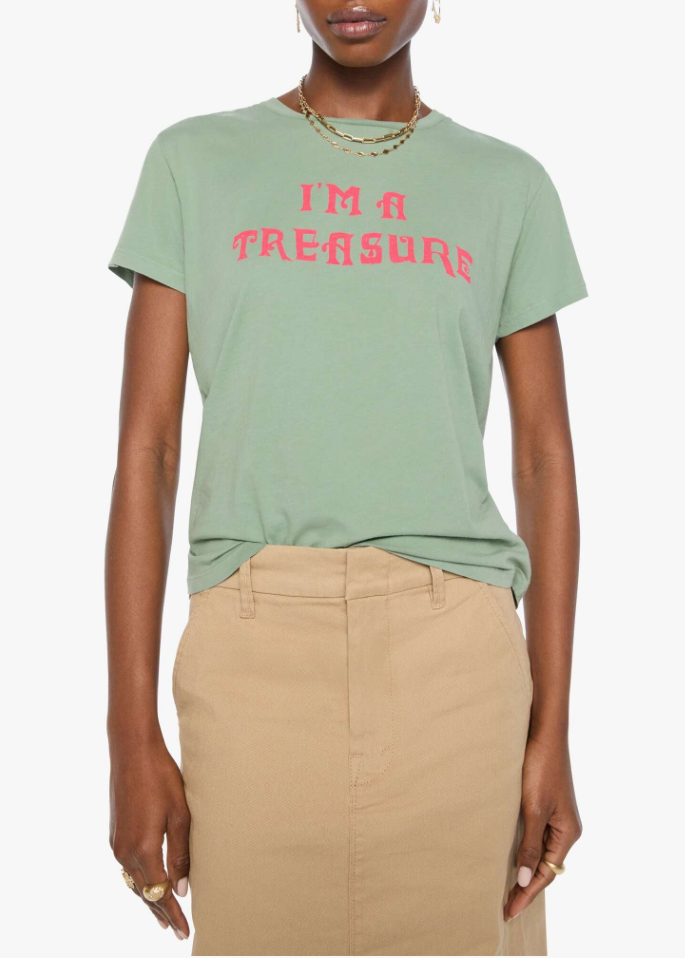A model wearing a sage green crewneck t-shirt with 'I'M A TREASURE' printed in pink across the chest, paired with a beige skirt, against a plain light gray background.
