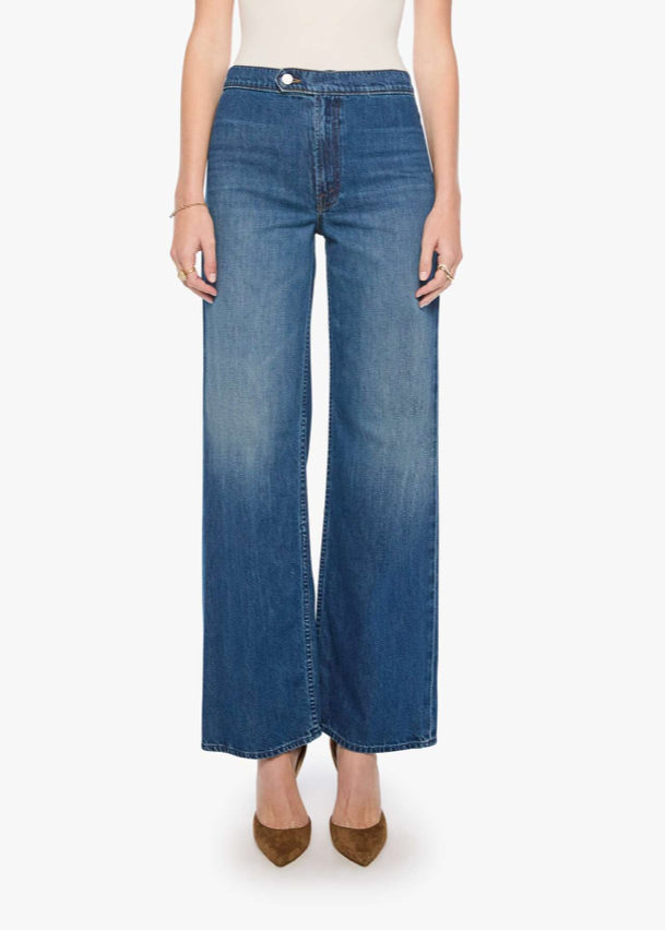 A model wearing a pair of medium wash blue wide-leg cropped jeans with a subtle vertical fade, paired with a white top and brown pointed-toe heels, against a plain white studio background.