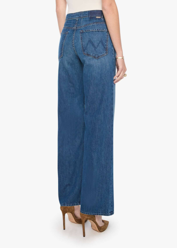 A model shown from the back wearing blue wide-leg jeans with a distinctive zigzag back pocket detail, paired with brown high heels against a plain white background.