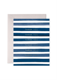 A thank you card with horizontal navy and medium blue watercolor stripes on a white background, with the words 'THANK YOU' printed in gold foil between the stripes. A light gray envelope is partially visible behind the card.
