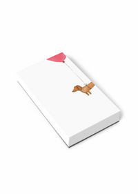 A white rectangular notepad shown at an angle on a black background, featuring a minimalist illustration of a tan dog holding a pink string balloon.