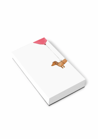A white rectangular notepad shown at an angle on a black background, featuring a minimalist illustration of a tan dog holding a pink string balloon.