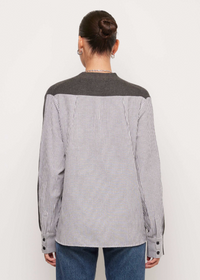 A model shown from the back wearing a long-sleeve button-up shirt with a gray and white vertical stripe body and solid dark gray shoulder yoke, paired with blue jeans against a plain off-white background.