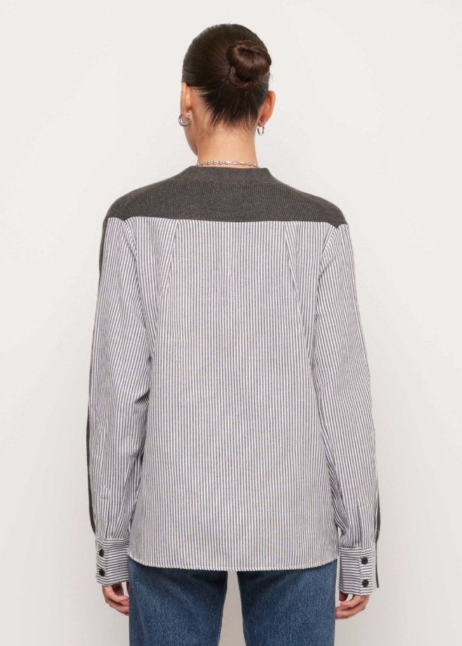 A model shown from the back wearing a long-sleeve button-up shirt with a gray and white vertical stripe body and solid dark gray shoulder yoke, paired with blue jeans against a plain off-white background.