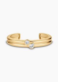 A gold-toned open cuff ring featuring two small clear gemstones, one round and one pear-cut, set against a plain white background.