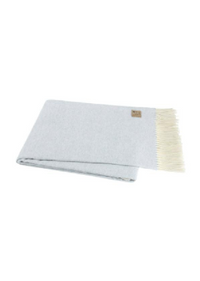 A folded light blue knit throw blanket with cream-colored fringe on one end and a small tan brand tag, shown on a plain white background.