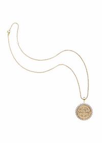 A gold chain necklace featuring a round pendant with a sunburst border of small clear stones and a central gold emblem, displayed on a clean white background.