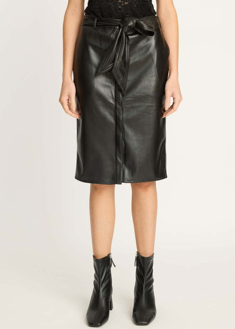 A model wearing a black faux-leather wrap midi skirt with a tie waist, paired with black ankle boots, shot against a plain light gray studio background.