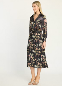 A woman modeling a long-sleeve midi shirt dress with a black base and a multicolor floral print, featuring a matching black belt, against a plain white studio background.