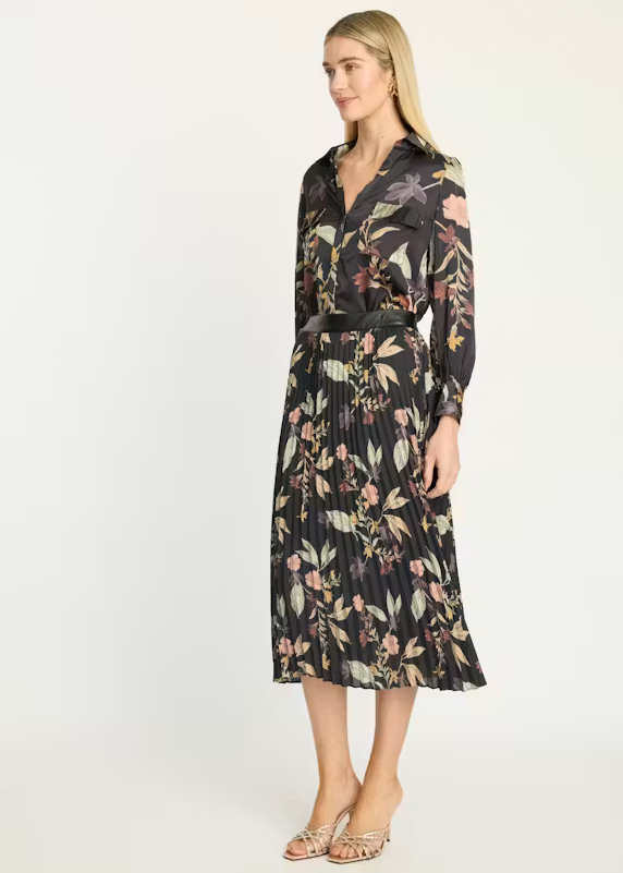 A woman modeling a long-sleeve midi shirt dress with a black base and a multicolor floral print, featuring a matching black belt, against a plain white studio background.