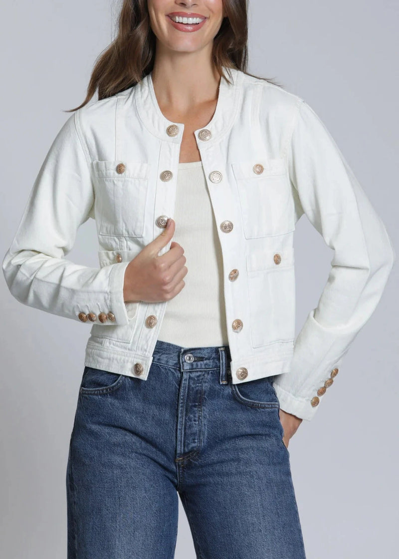 Woman wearing a white denim jacket with gold buttons and blue jeans on a gray background