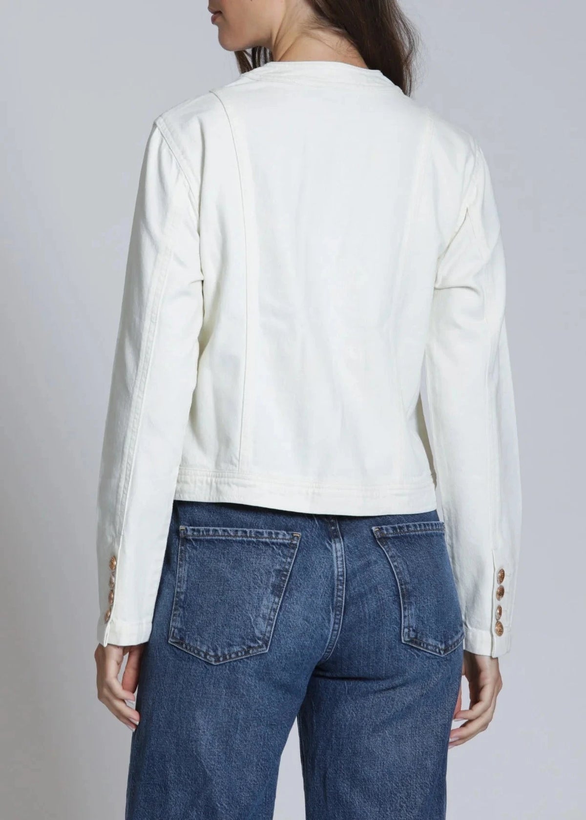 Person wearing a white jacket with button details and blue jeans on a plain background