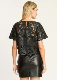 A woman shown from the back wearing a black lace short-sleeve top with a floral lace overlay and a black faux-leather mini skirt, against a plain light background.
